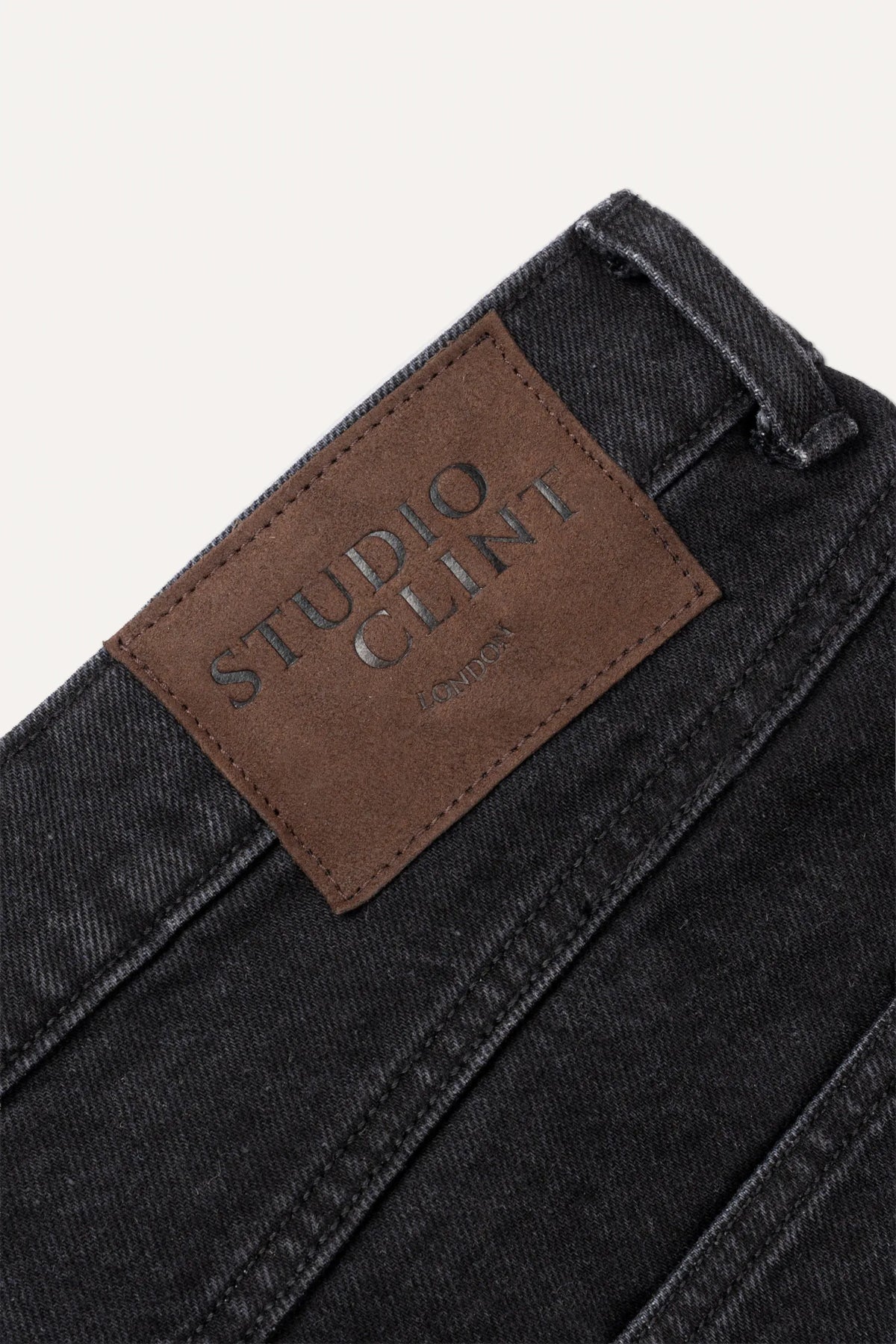 A close-up of coal black denim jeans showing the waistband, button fly, and front pocket stitching.