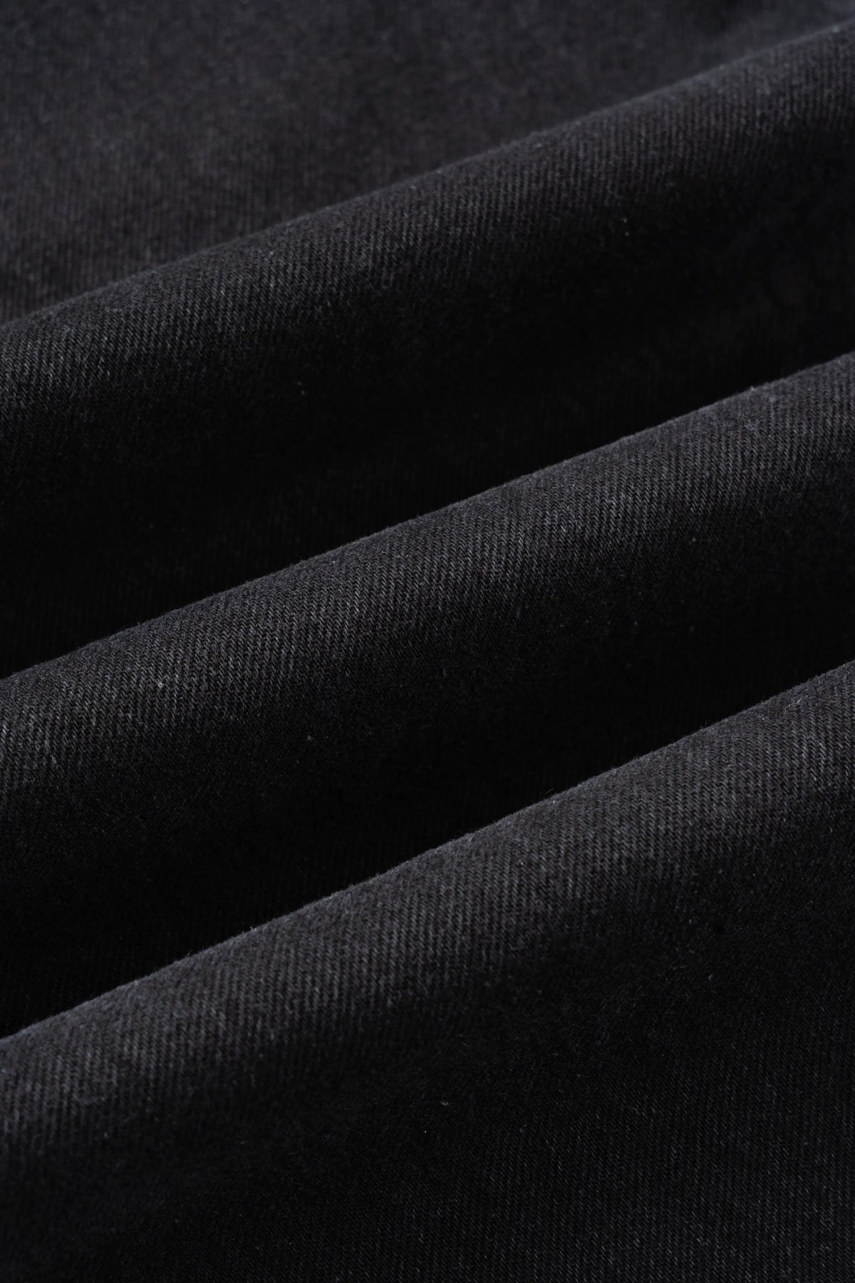 A close-up of the front pockets and belt loops on coal black denim jeans.