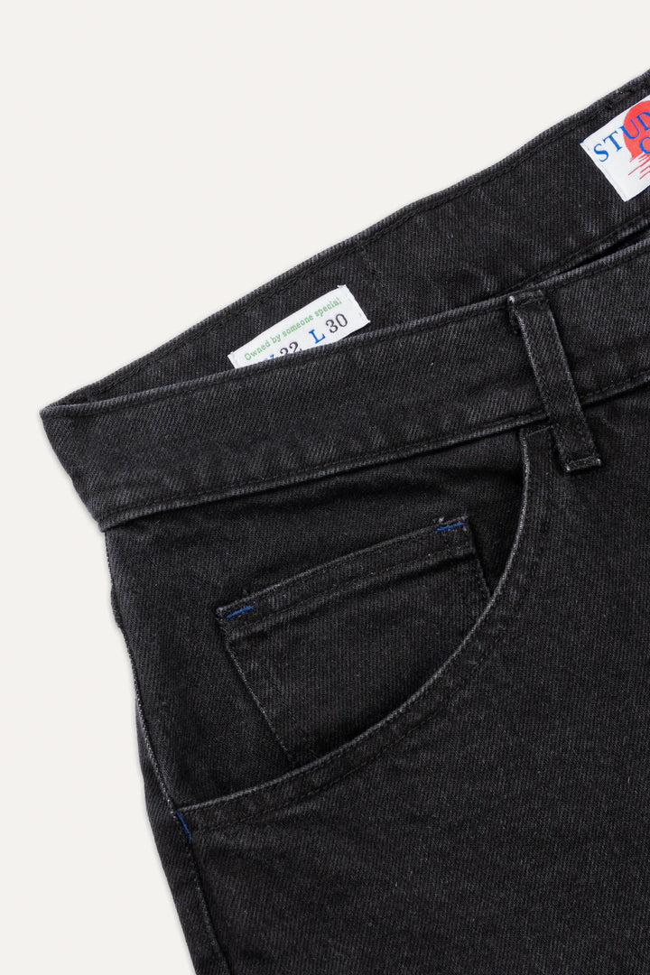 A close-up of the rear waistband and belt loops on coal black denim jeans.