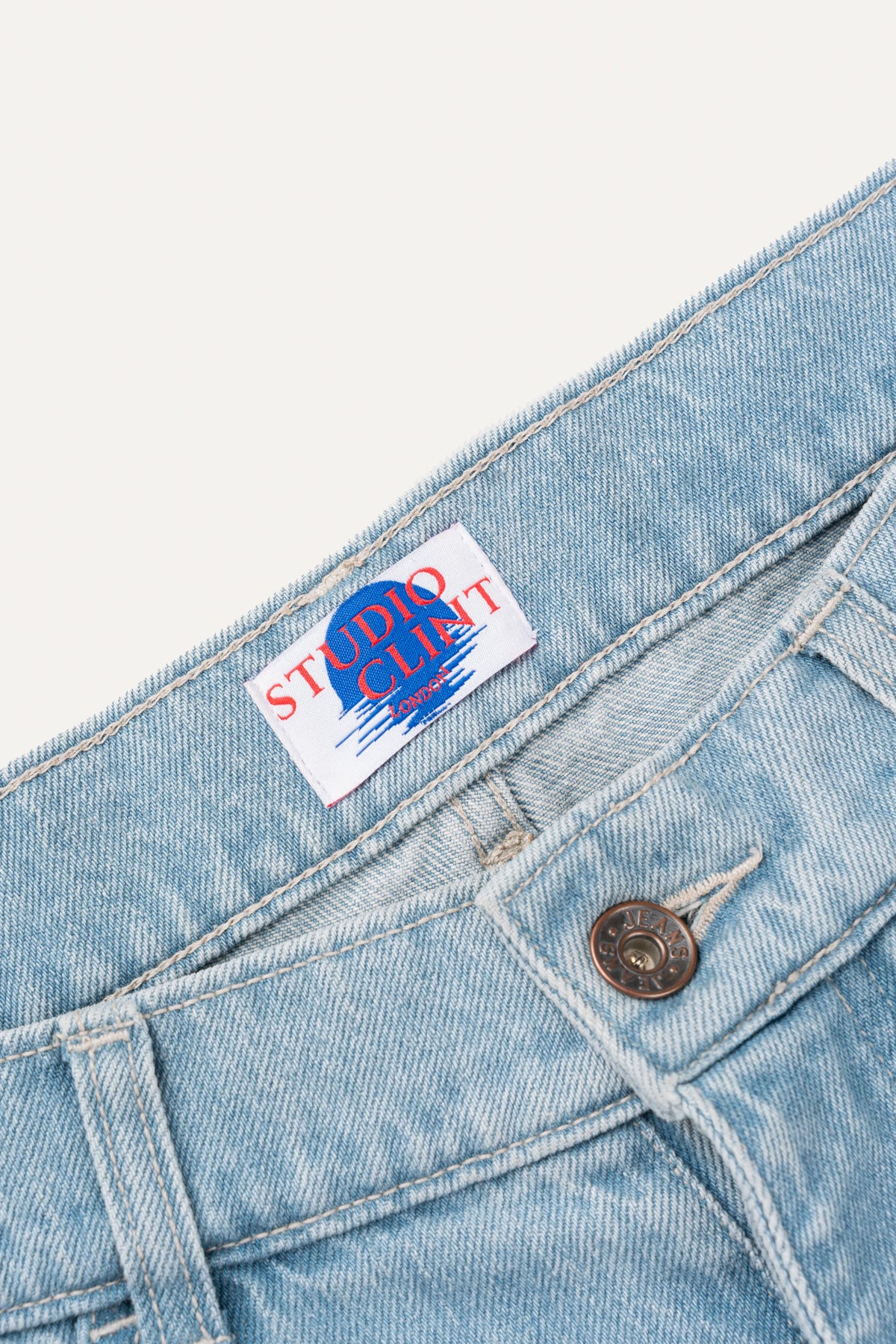 The back pocket detail of light blue denim jeans, showing the signature bartack stitching.