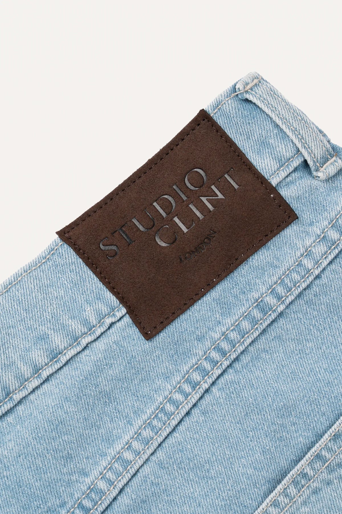 A close-up of light blue denim jeans showing the waistband, button fly, and front pocket stitching.
