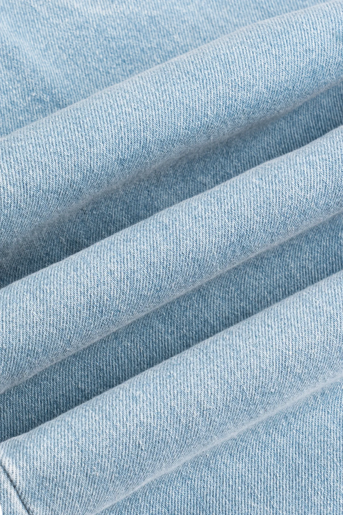A close-up of the front pockets and belt loops on light blue denim jeans.