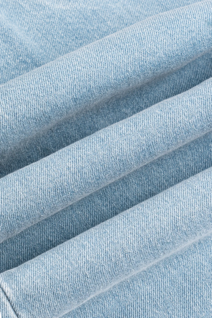 A close-up of the front pockets and belt loops on light blue denim jeans.