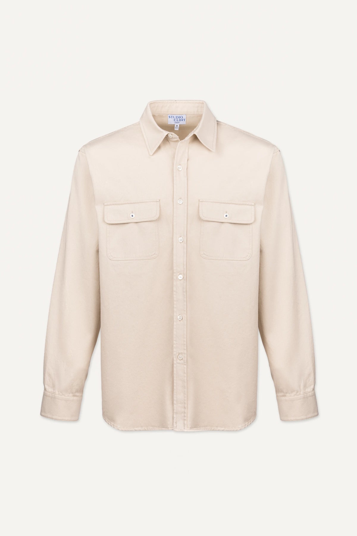 A light beige long-sleeve button-up shirt with two buttoned chest flap pockets, displayed on a clean, solid off-white background.
