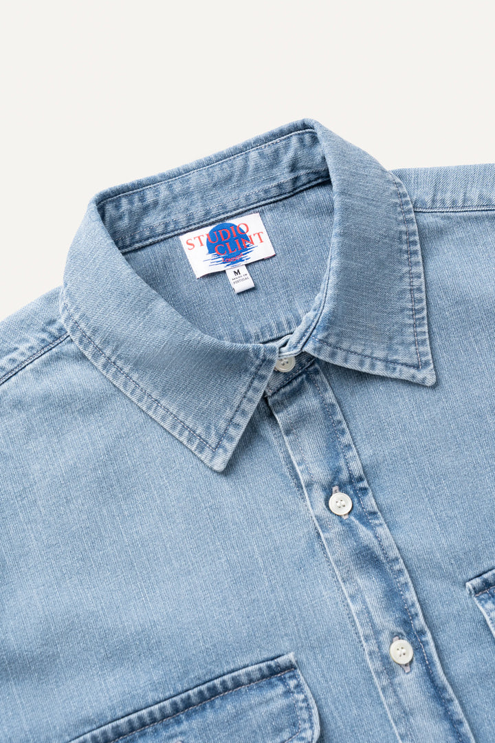 Close-up of a light blue denim button-down shirt collar with a visible neck label reading 'Studio Clint'.