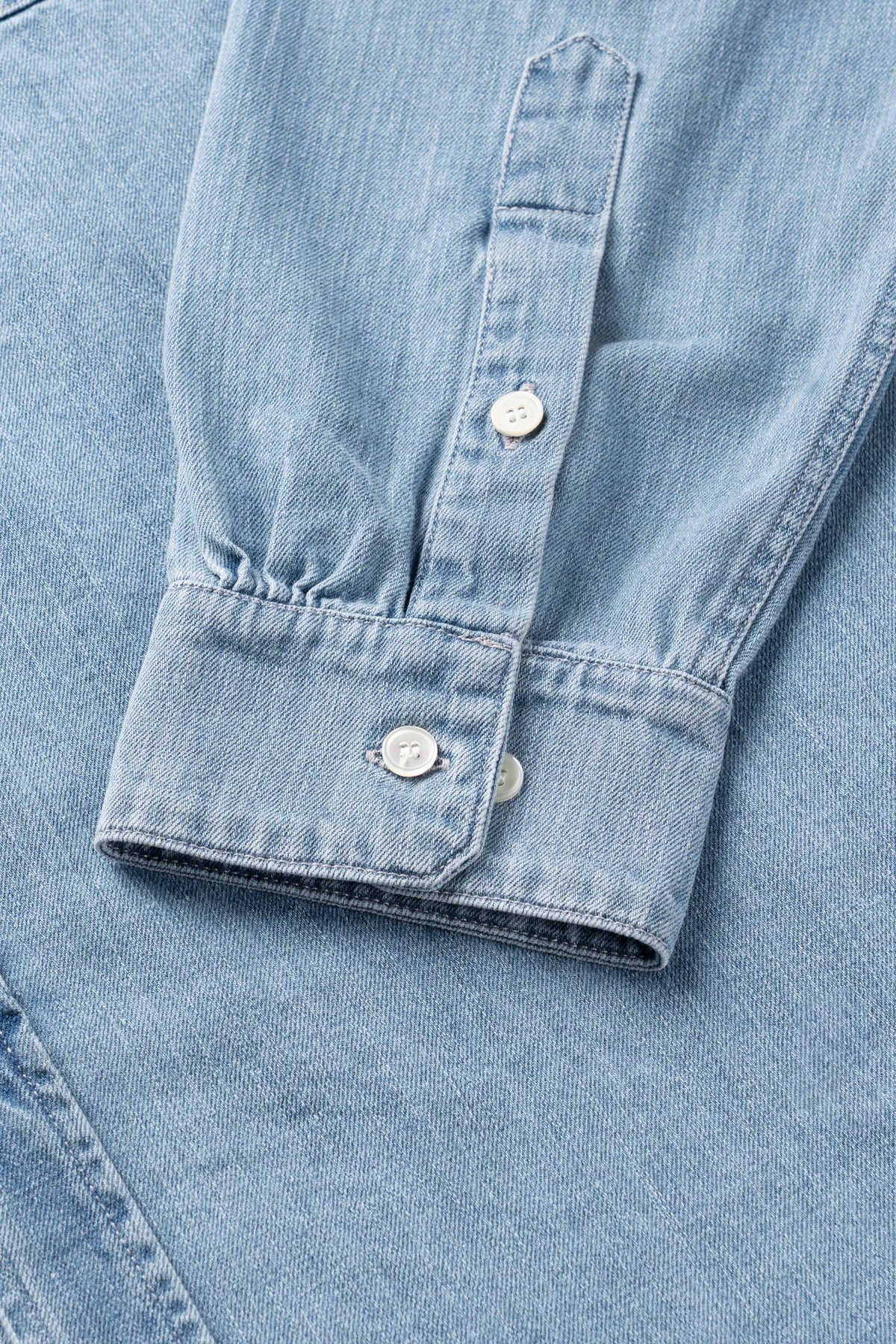Close-up of a light blue denim shirt sleeve showing the buttoned cuff and front placket.