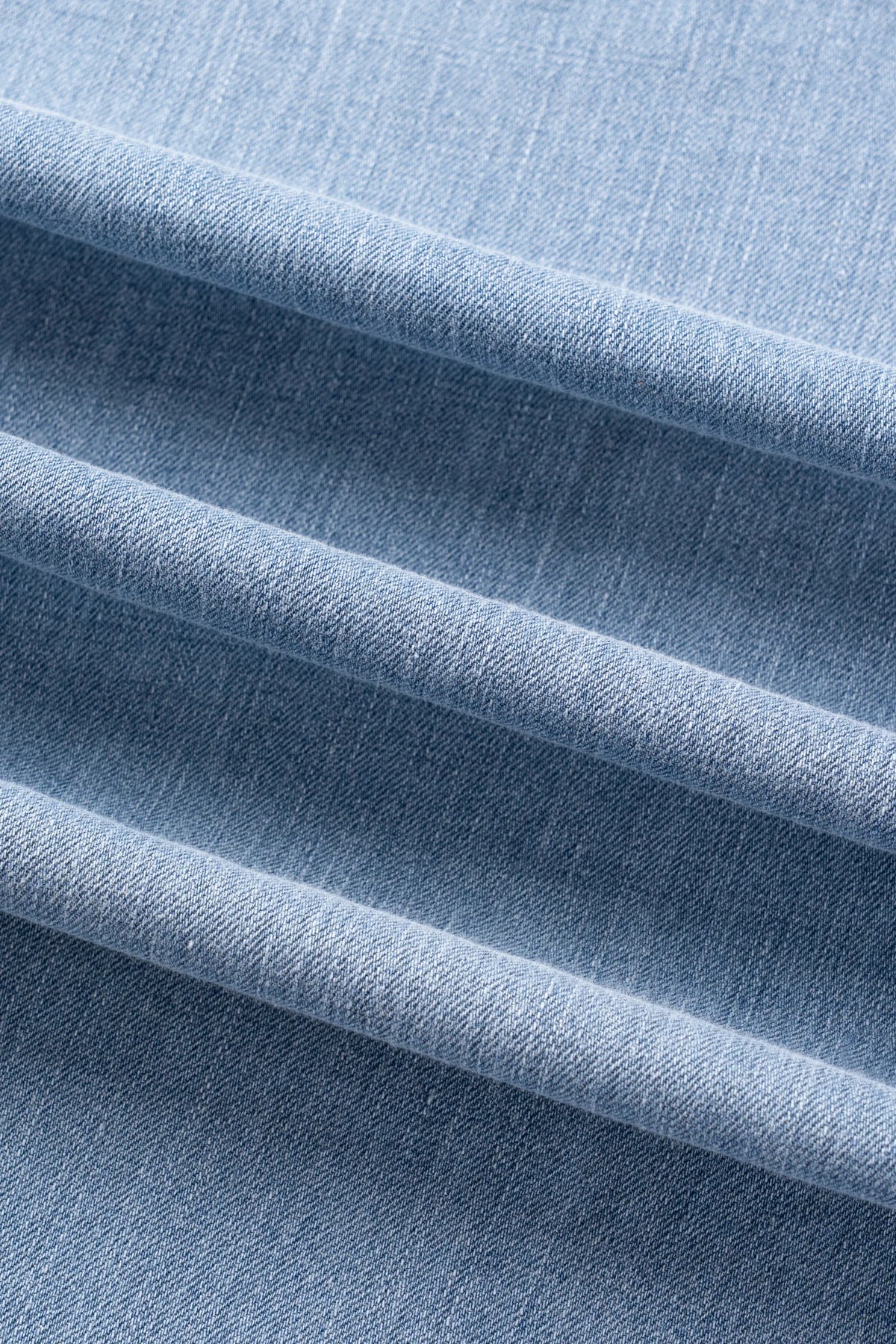 A close-up of light blue woven fabric with soft diagonal folds showing the texture and weave.