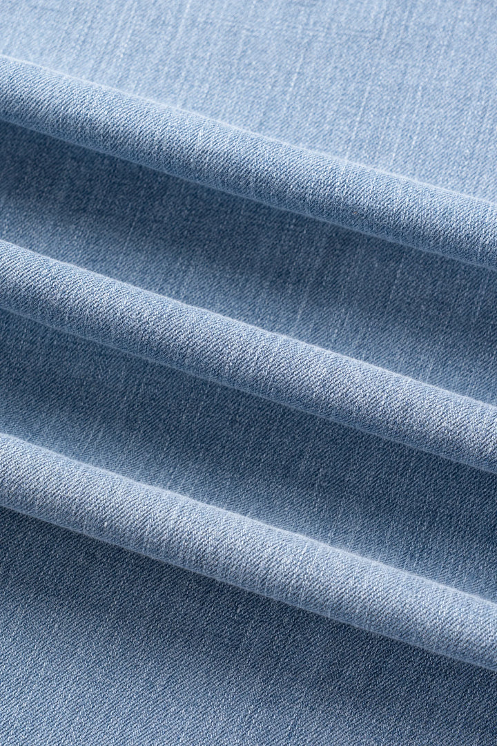 A close-up of light blue woven fabric with soft diagonal folds showing the texture and weave.