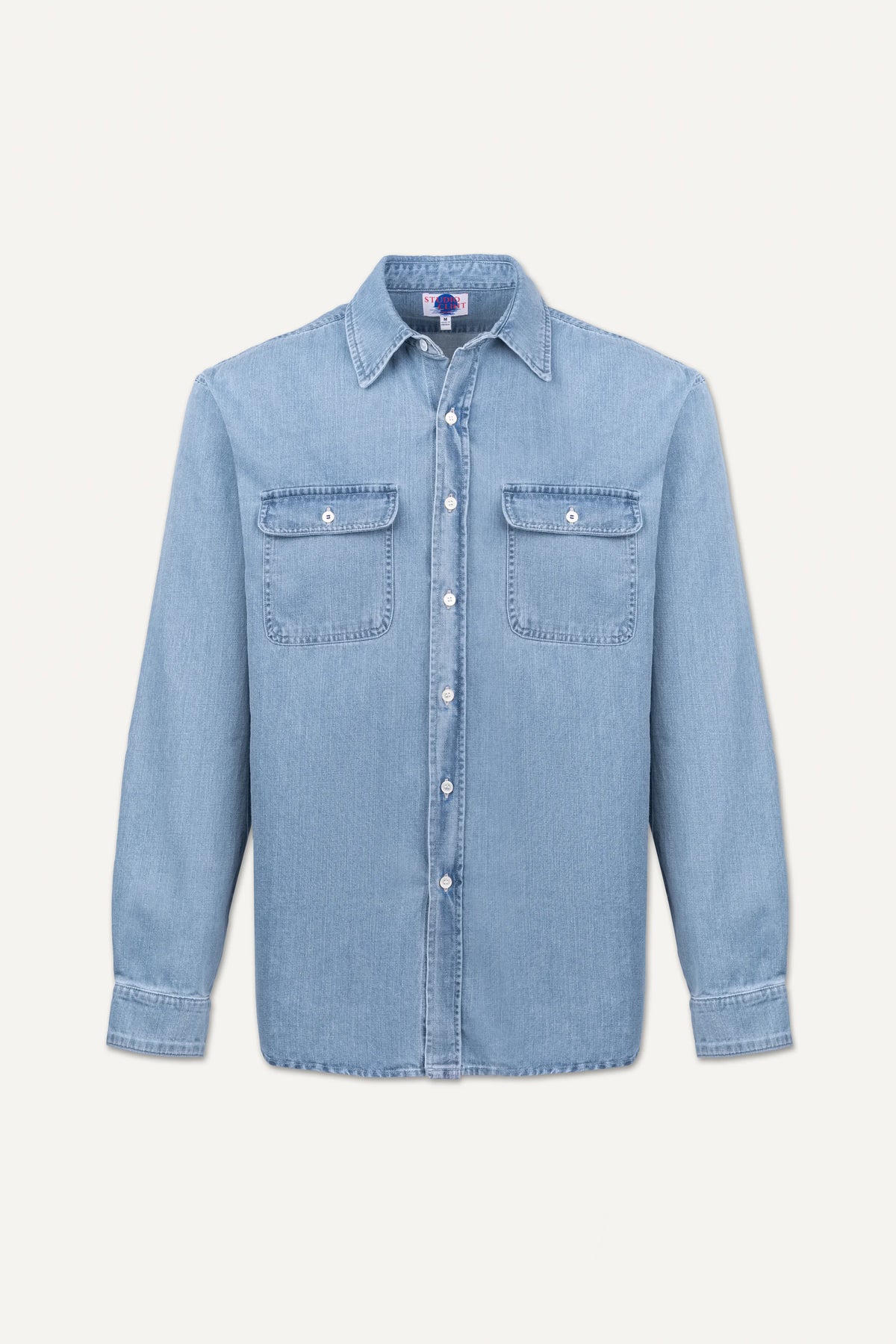 A light blue denim long-sleeve button-up shirt with two buttoned chest pockets, displayed flat against a light off-white background.