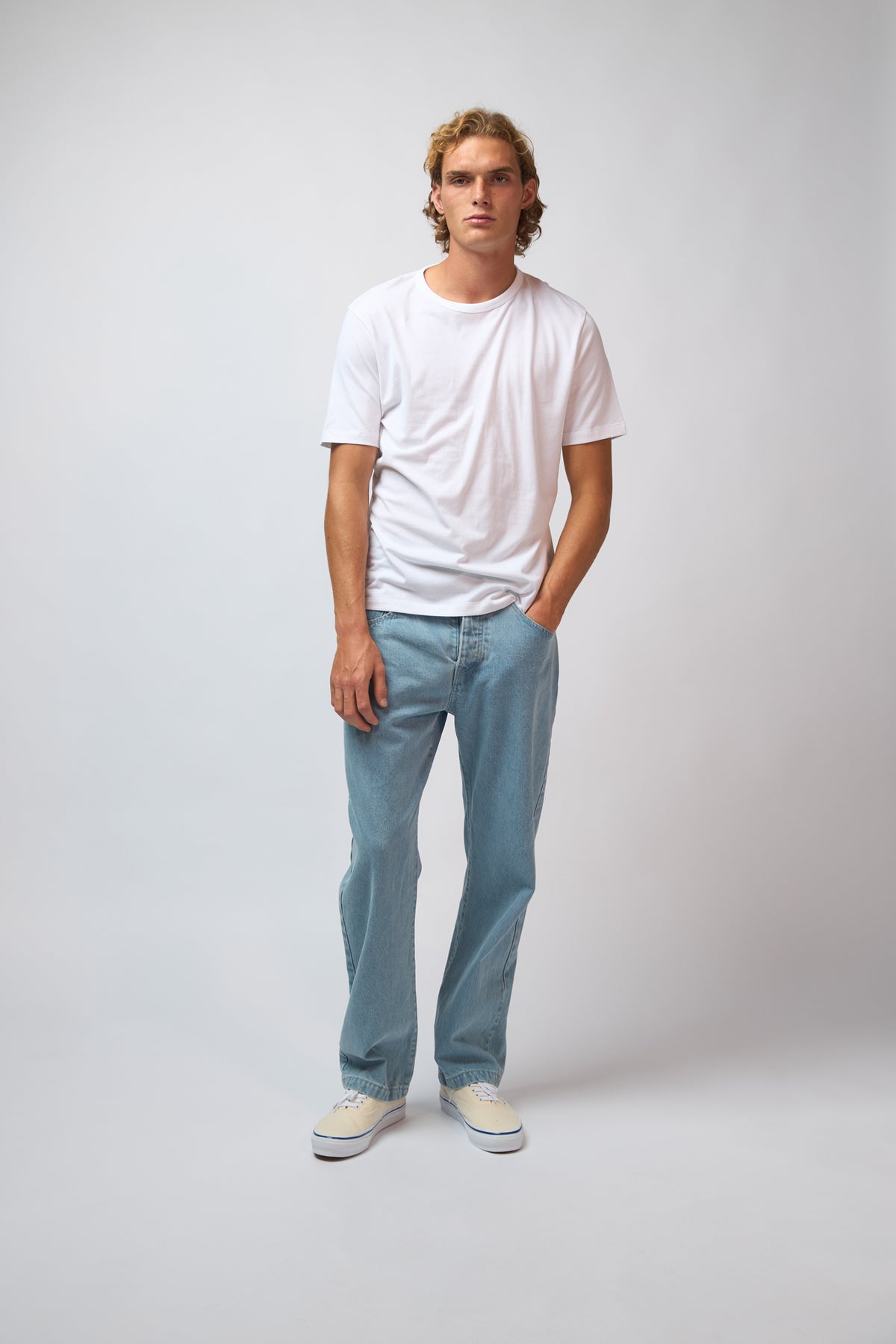 A man wearing light blue denim jeans with a navy jacket, standing against a plain grey studio background.