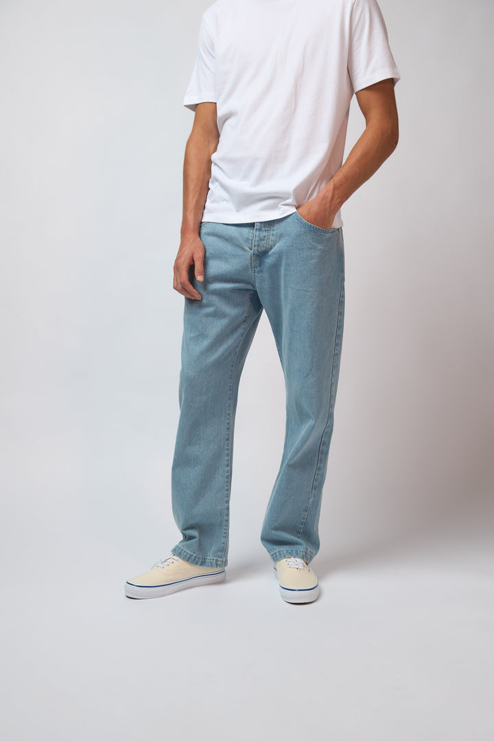A man wearing light blue denim jeans with a white t-shirt, standing against a light grey studio background.