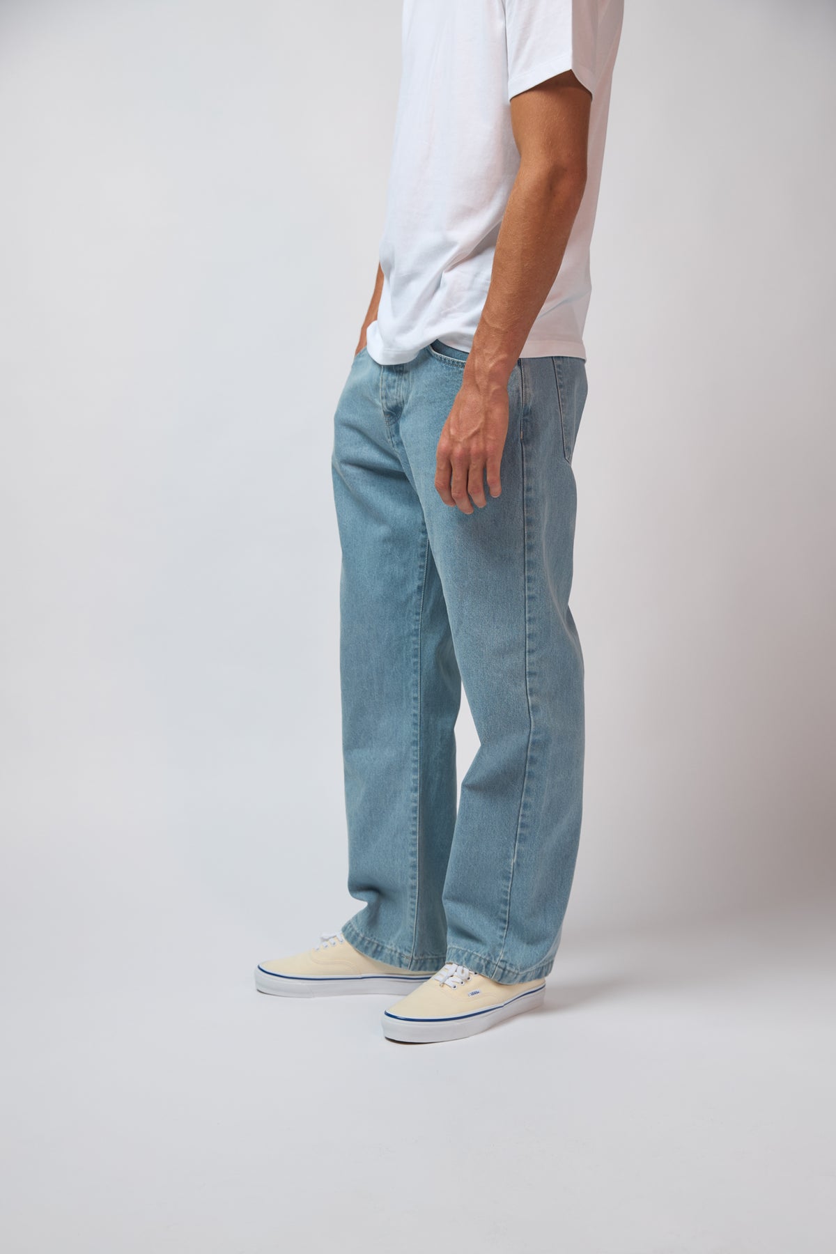 A man wearing light blue denim jeans with a white t-shirt, standing against a plain grey studio background.