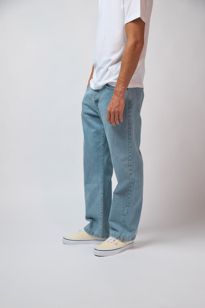 A man wearing light blue denim jeans with a white t-shirt, standing against a plain grey studio background.