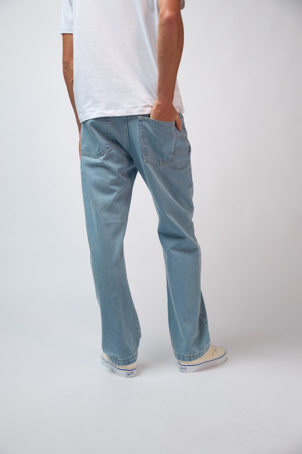 A man wearing light blue denim jeans styled with a navy jacket, standing against a plain grey studio background.