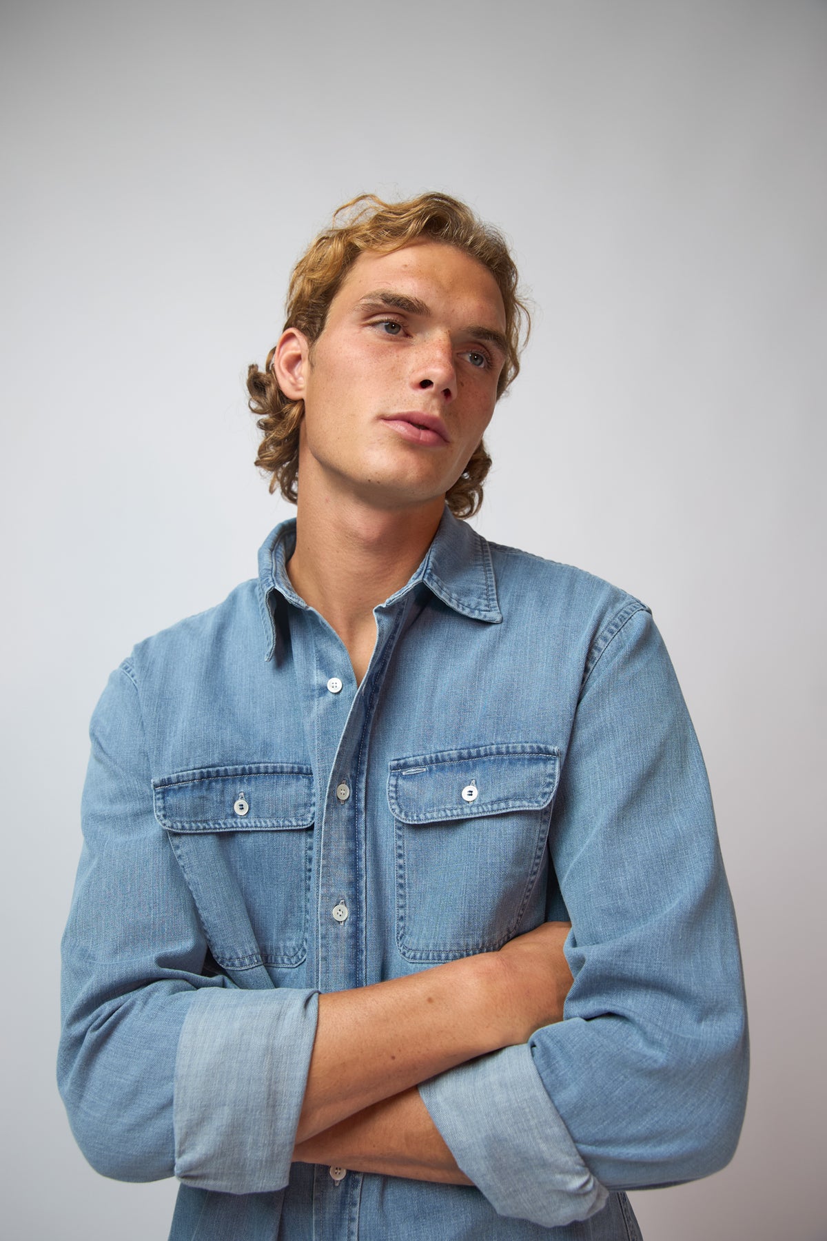 A man wearing the washed denim double pocket shirt, shown from the side against a plain grey studio background.