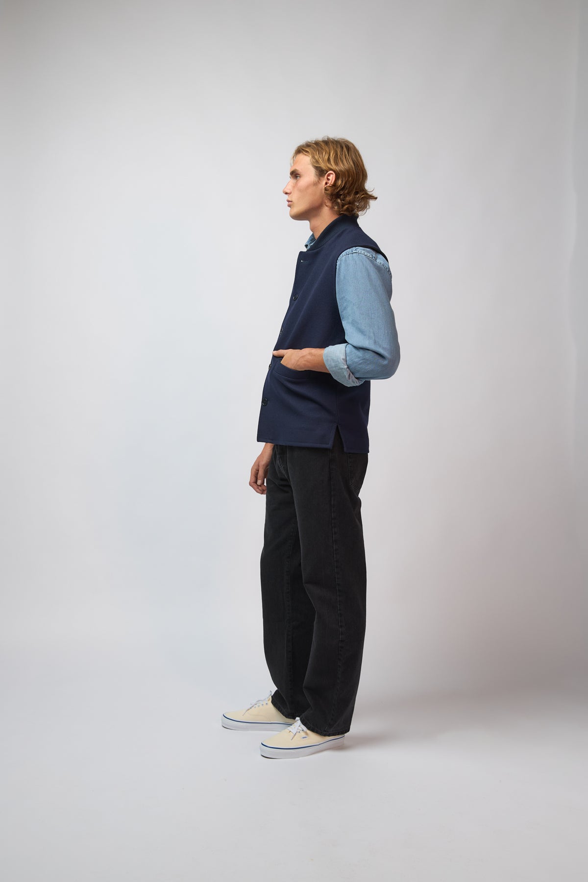 A man wearing a midnight navy loden-wool vest, shown from a three-quarter angle against a plain grey studio background.