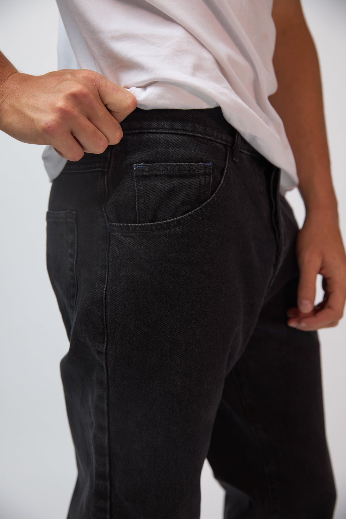 A man wearing coal black denim jeans styled with a navy jacket, standing against a plain grey studio background.