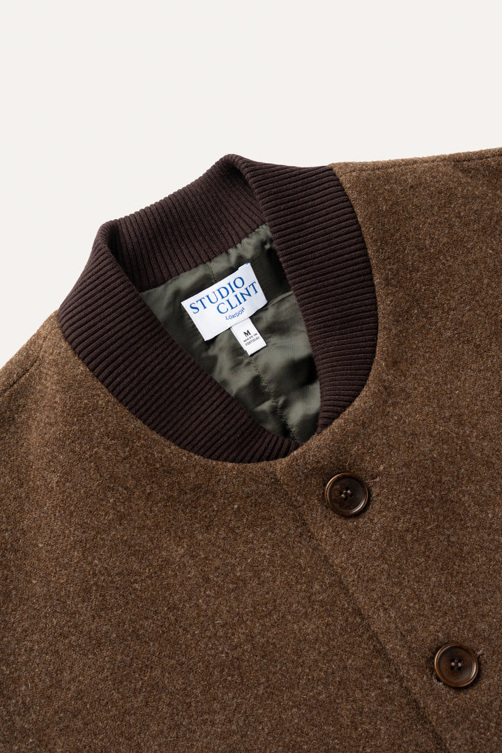 Close-up of a brown wool-blend jacket with a dark brown ribbed knit collar and a visible Studio Cliff brand label.