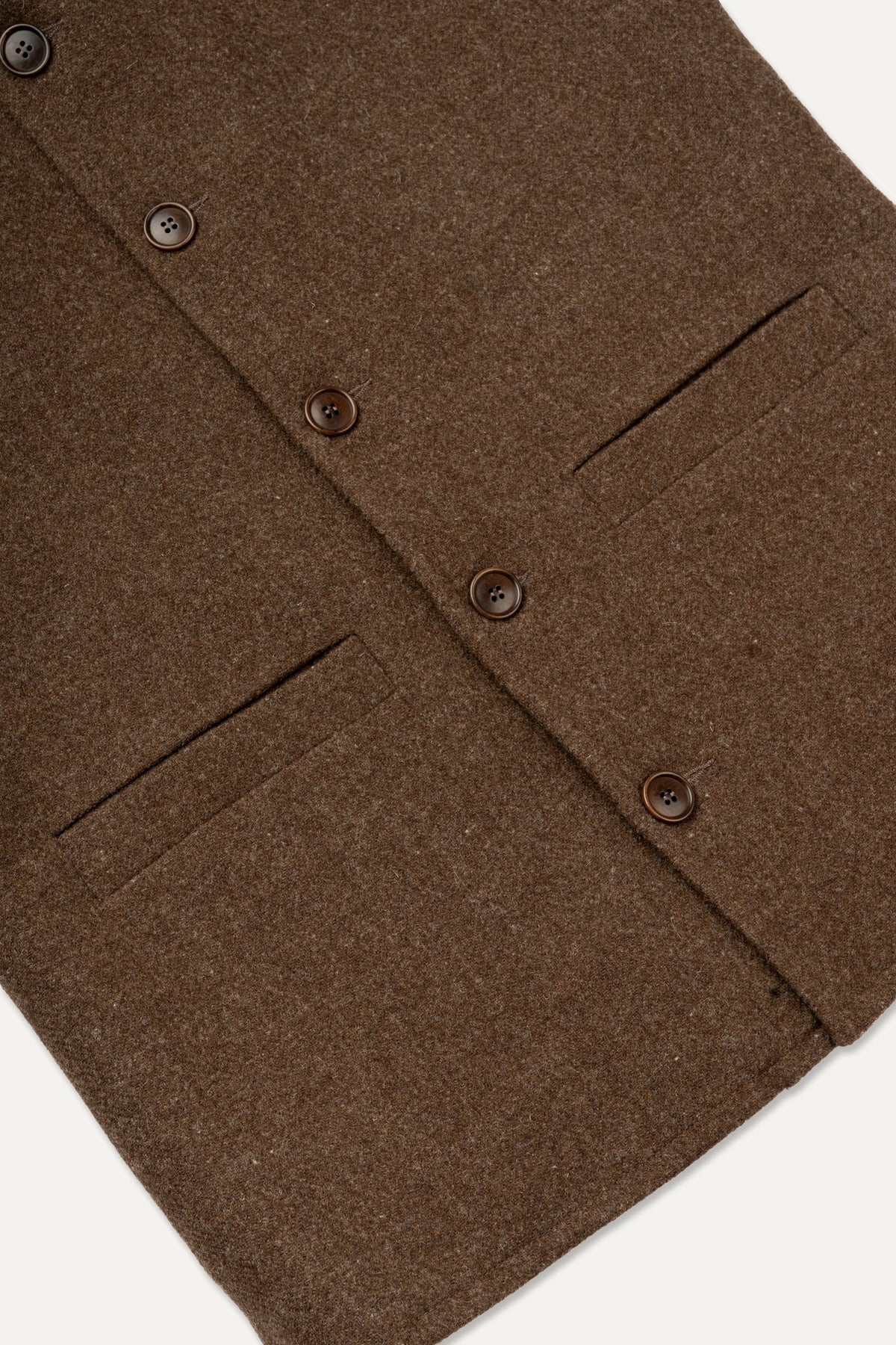 Close-up of a brown wool-blend jacket or coat showing the buttoned front, flap pockets, and textured fabric against a light neutral background.