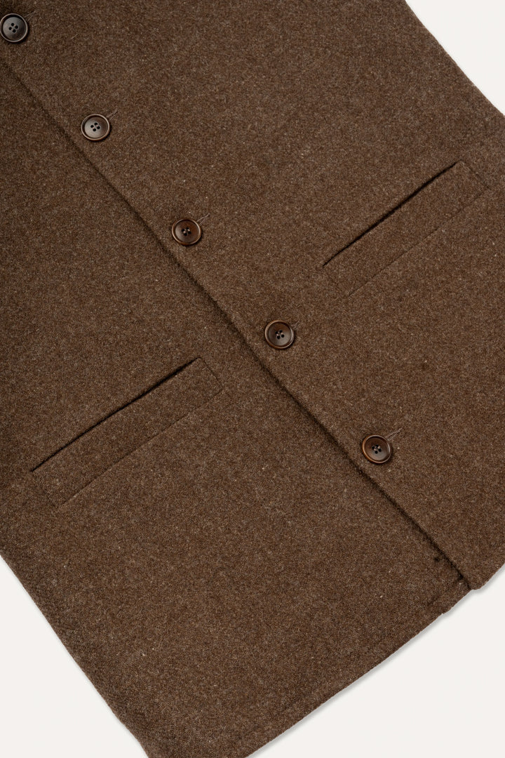 Close-up of a brown wool-blend jacket or coat showing the buttoned front, flap pockets, and textured fabric against a light neutral background.