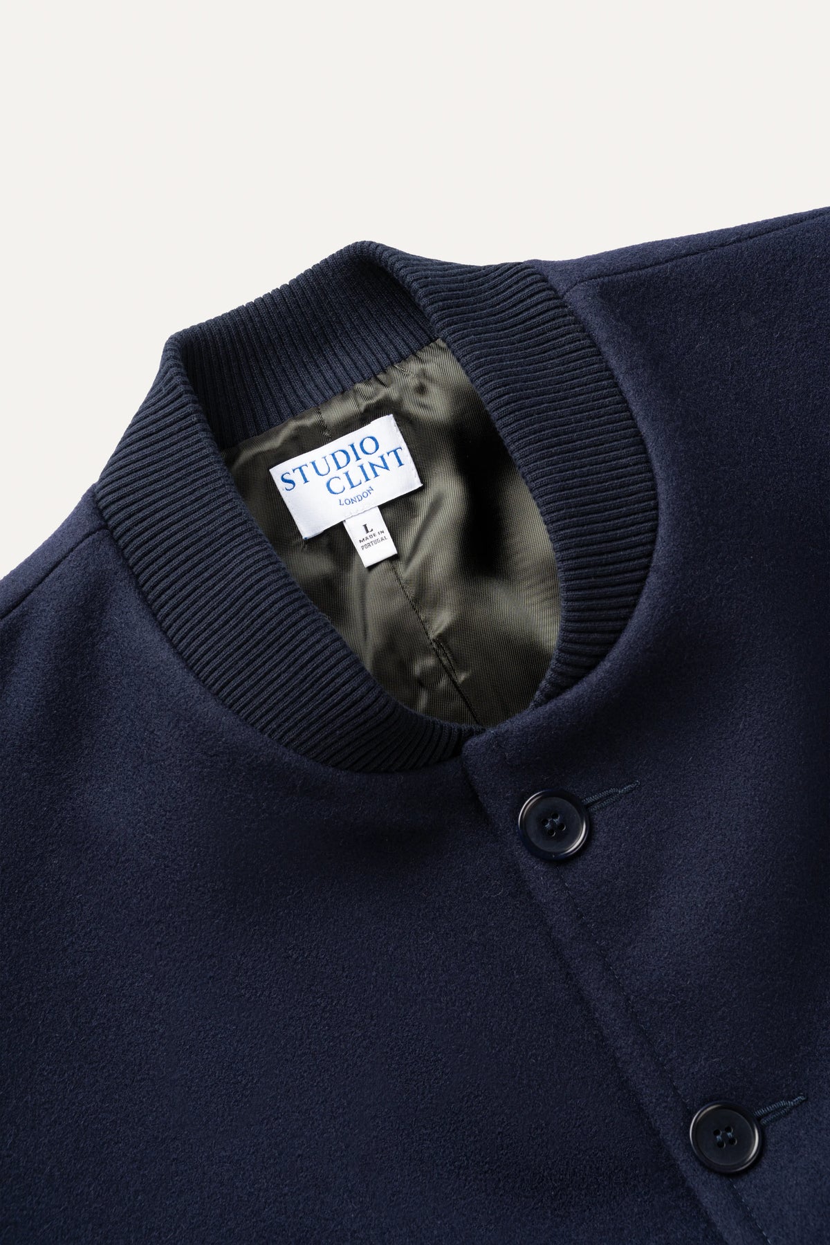 Close-up of a navy blue knit cardigan sweater by Studio Clint, showing the ribbed collar, black buttons, and the brand label inside the neck.