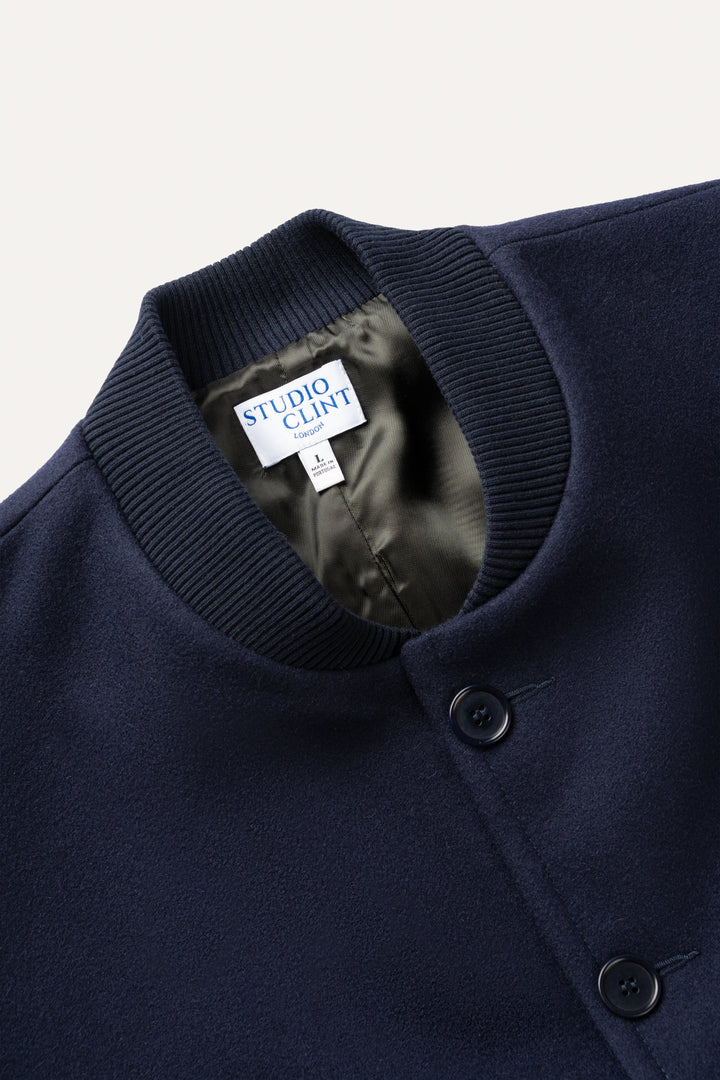 Close-up of a navy blue knit cardigan sweater by Studio Clint, showing the ribbed collar, black buttons, and the brand label inside the neck.